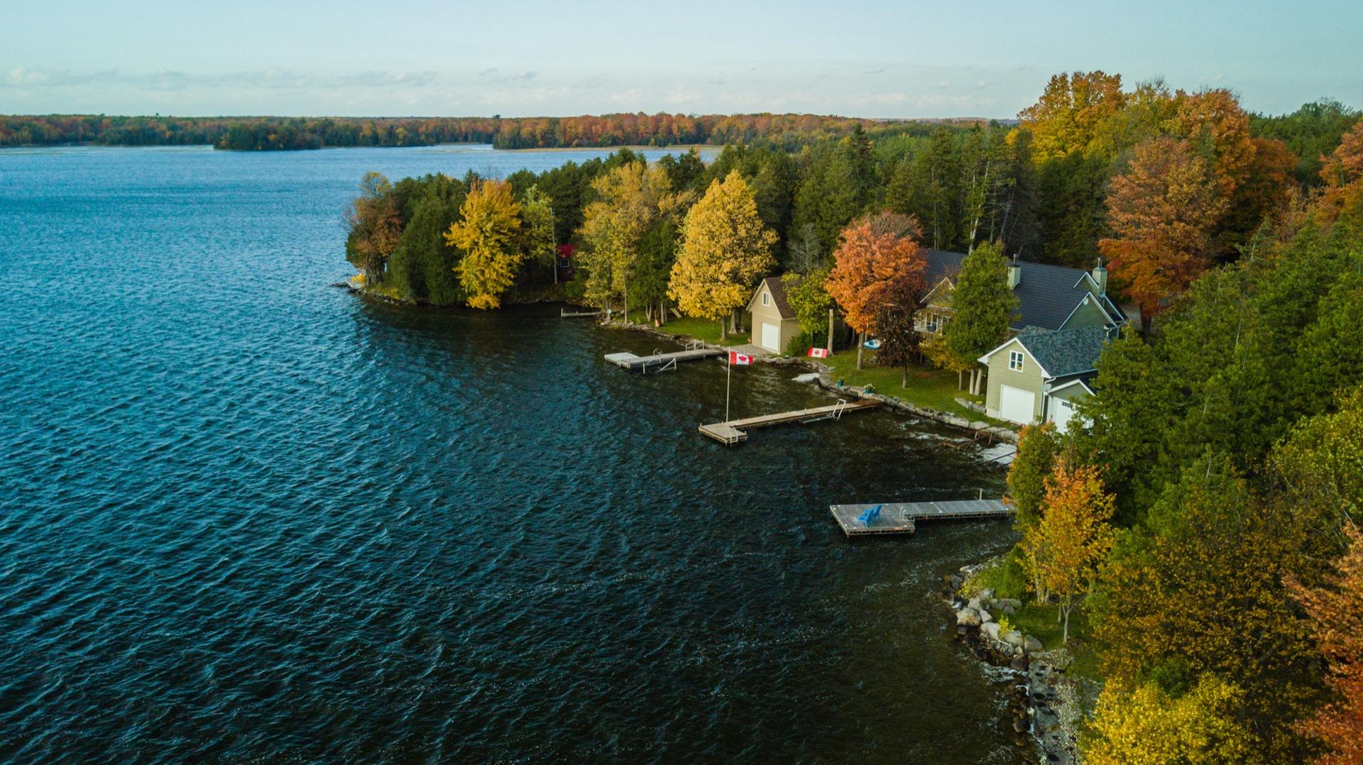 Aerial view of a waterfront cottage with a dock and boathouse, surrounded by autumn maples